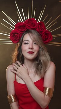 Vertical 4K video. 60 fps. Mature white woman with DIY golden halo crown, rose on head, red dress, make up, gold bracer, bare shoulder looks at camera. Smoke, fog. Concept of Middle Ages, pray, beauty