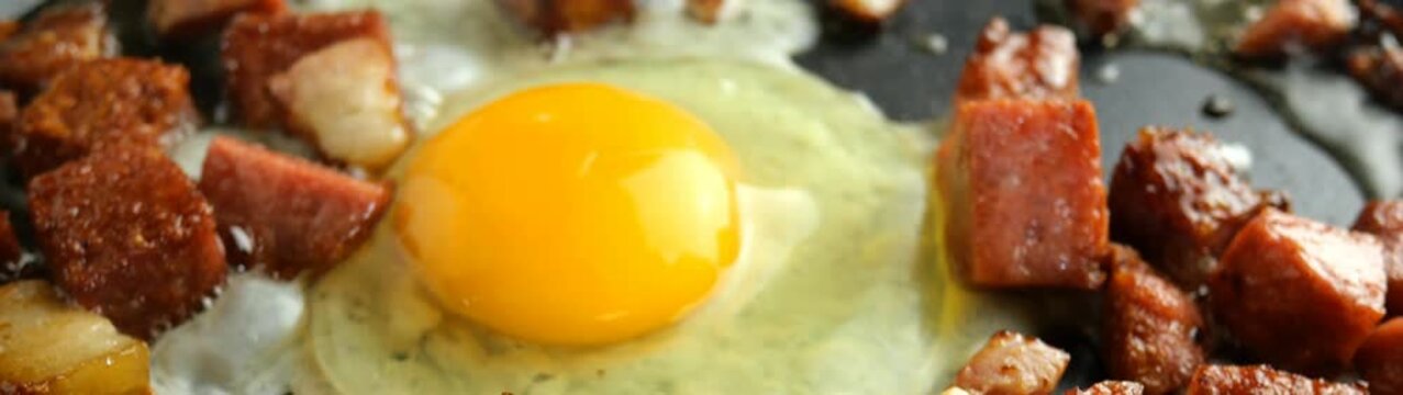 Egg yolk frying with diced spam in a hot skillet sizzling savory breakfast simple home cooked morning meal.