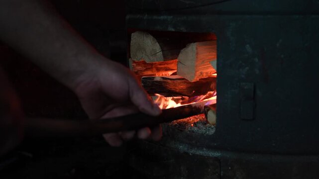 Person adding firewood to wood burning stove with glowing flames