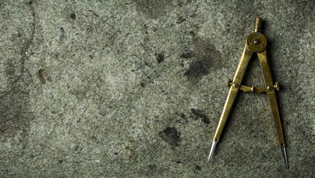 Vintage brass drawing compass tool on rough textured grey felt background