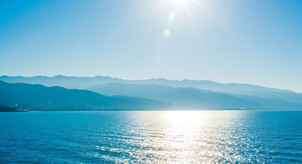 Sunlight reflecting on calm ocean surface against distant blue coastal mountains with reflection mountains landscape coastline outdoors