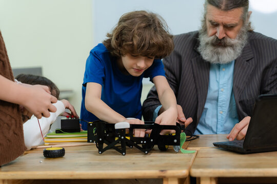 Close-up of a schoolboy assembling a robot kit with his senior teacher in a STEM technology classroom.