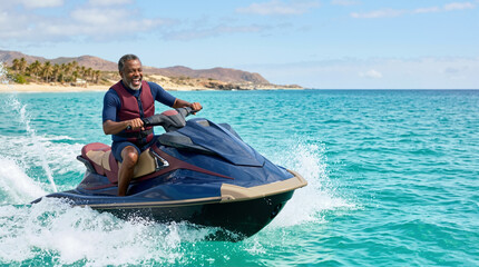 Obraz premium Joyful senior Black man riding jet ski on turquoise ocean water. Happy older male enjoying summer vacation water sports. Active lifestyle and travel concept