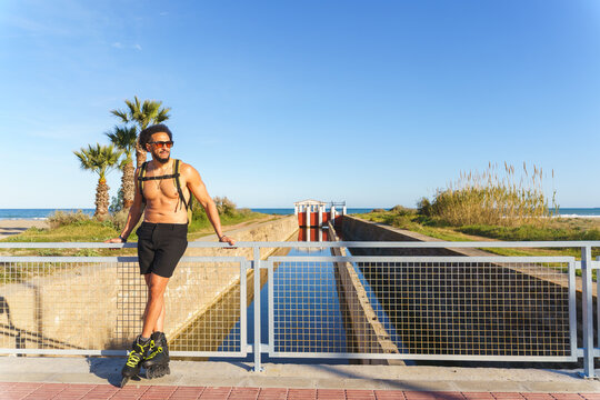 Shirtless latino man with rollerblades enjoying outdoor activity by a beach canal