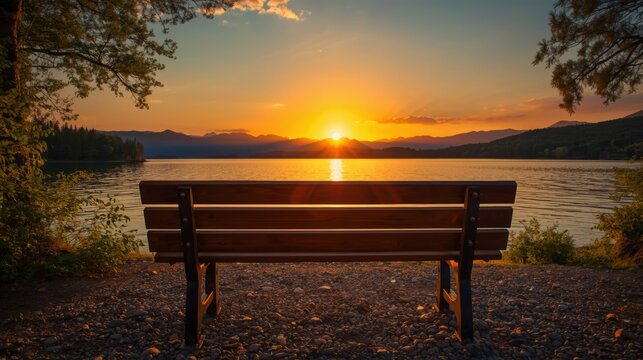 Empty wooden park bench facing a beautiful lake at sunset with orange sky and calm water reflection