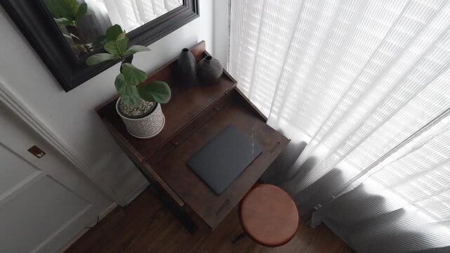 Minimalist home office setup with closed laptop on vintage wooden desk by sunny window.