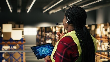 Fototapeta premium Black woman call center operator using headset and AI technology on tablet, working on warehouse platform, Artificial intelligence and neural networks tools for order fulfillment.