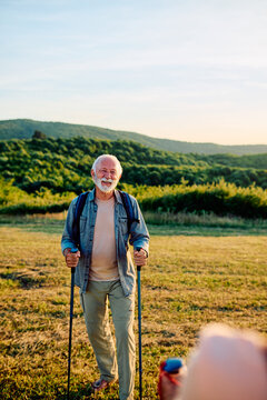 Smiling senior man enjoying a healthy active lifestyle and nature while walking with trekking poles in a mountain landscape