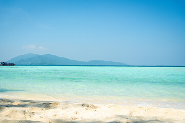 Obraz premium Serene Tropical Beach with Clear Shallow Waters and Mountain Backdrop