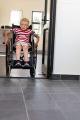 Naklejka premium Boy aged six to eight pushing wheelchair with hand rims through home doorway, wearing striped shirt