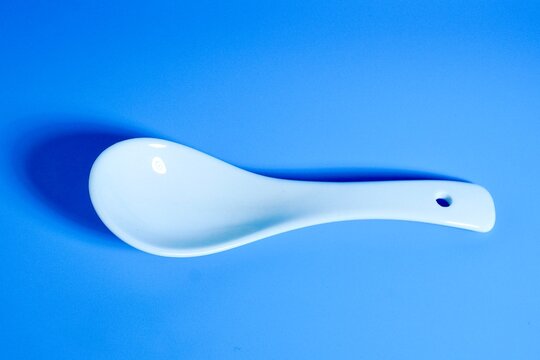One white ceramic soup spoon isolated on horizontal blue background.