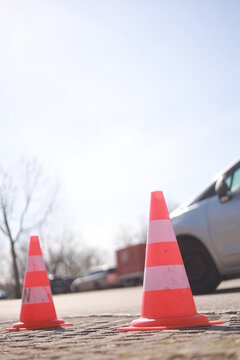 Two orange and white traffic cones are on the ground in front of a silver car