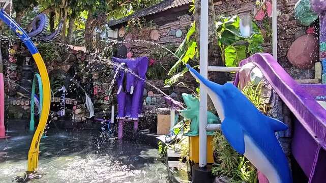 Colorful animal fountain playground in a kids pool, featuring water jets from dolphin, frog, and elephant sculptures surrounded by tropical plants and playful d&eacute;cor.