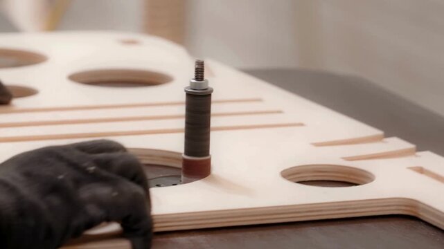 Closeup of a woodworker using a spindle sander to smooth the edges of a circular hole in plywood