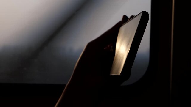 Closeup shot of smartphone, blurred train window on background. Passenger spend time by watching film or reading book using mobile device, high contrast slow motion shot