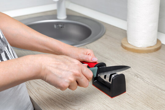 A housewife sharpens a kitchen knife. sharpening a kitchen knife in the home kitchen. manual sharpener for a kitchen knife. manual knife sharpener. 