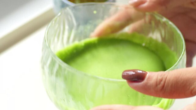 4K Close up of hand using traditional bamboo whisk to mix green matcha tea powder in clear glass bowl, Concept of traditional Japanese tea ceremony preparation and healthy lifestyle.