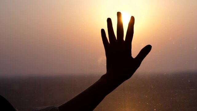 Dreamy passenger put hand on train window, hold against shining sun, bright beam on background, silhouetted palm lie on glass. High speed train ride at evening time