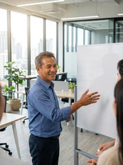 Fototapeta premium Middle aged businessman presenting at whiteboard in modern office