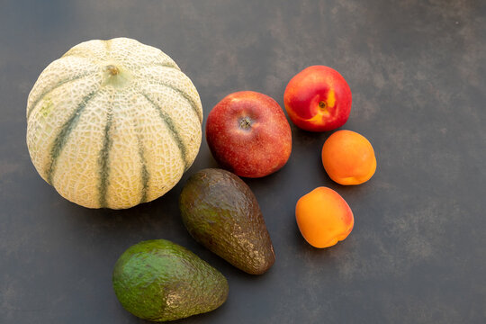 Frisches Arrangement mit Melone, Avocado und gesunden Zutaten auf dunklem Hintergrund