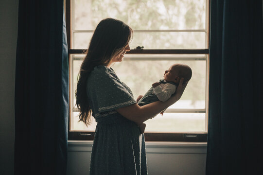 Mother smiling lovingly at her newborn baby framed in window