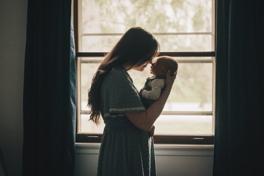 Mother touching her nose to her newborn baby's nose by window light