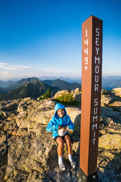 Happy kid rests at a mountain summit marker