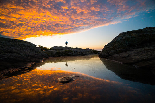 Hiker silhouetted on rocks watching fiery sunset