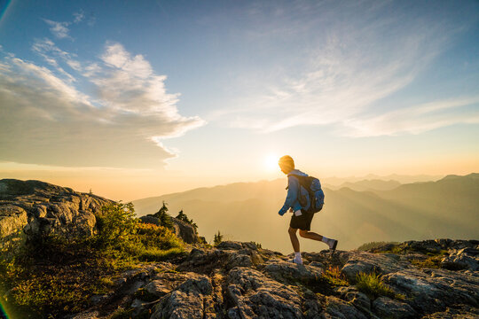 Young hiker runs along a mountain summit at sunset