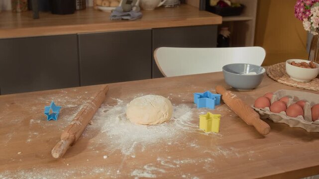 Handheld shot of raw dough, wooden rolling pins, star-shaped cookie cutters, and fresh eggs on flour-dusted kitchen table. Clip is perfect for family cooking blogs or holiday baking advertisements