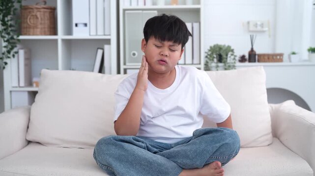 Young child experiencing toothache, tooth decay, childhood dental pain. The child facial expression, hand gently pressed against the cheek, dental care, children oral health, pediatric dental check-up