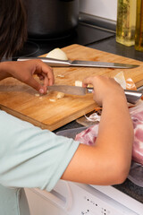 Obraz premium Child hands cutting garlic cloves on wooden cutting board