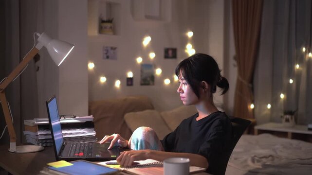 Young woman was intently working on laptop and taking notes on a notebook at bedroom desk  in the quiet late night 