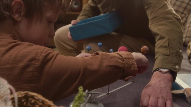 Handheld shot of senior man and child assembling solar system model toy together. Clip is ideal for family bonding, science education, and holiday toy marketing campaigns