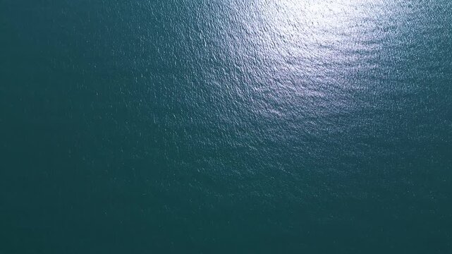 Aerial top down view of a blue sea water surface with sun reflection