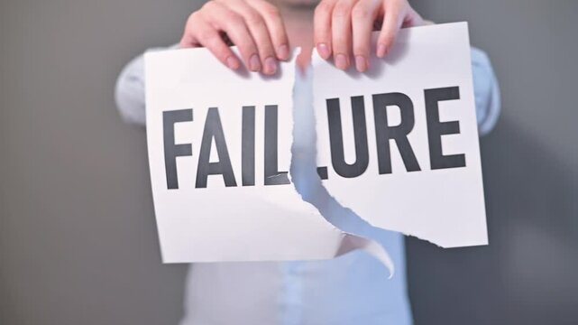 A person stands against a plain background, holding up signs that read failure. They proceed to tear and discard these signs, showcasing a process of letting go and moving forward