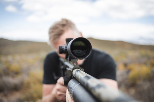 Person aiming rifle with telescopic scope outdoors
