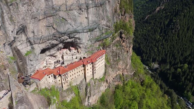 aerial shot flying towards Sumela Monastery nestled within high rocky mountain cliffs. Ancient religious complex landscape during a bright summer day in Trabzon region, Turkey.