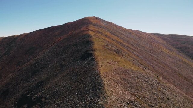 Aerial drone footage of a lone hiker pushing uphill on a steep alpine trail along the Continental Divide Trail.