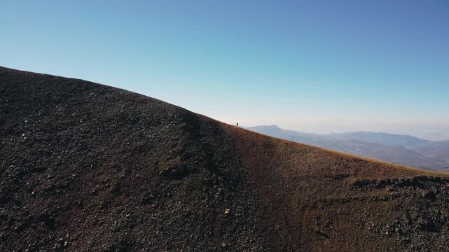 Aerial drone footage of a lone hiker pushing uphill on a steep alpine trail in remote wilderness.