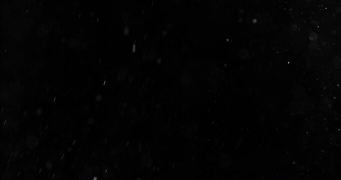 Super slow motion falling snow or dust particles isolated on a black background. Abstract atmospheric SFX overlay with floating debris, cinematic texture and dark visual effect.