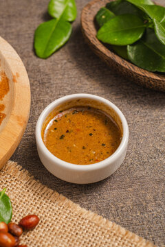 sambal pecel served on a table with a base and served on a wooden plate with a spoon, leaves, chilies ,peanuts and spices as decoration.
