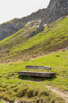 wooden park bench on slope near blue alpine lake in spring between forested mountains. hiking area in Bregenz forest, Vorarlberg, Austria. holiday destination for hike and skiing