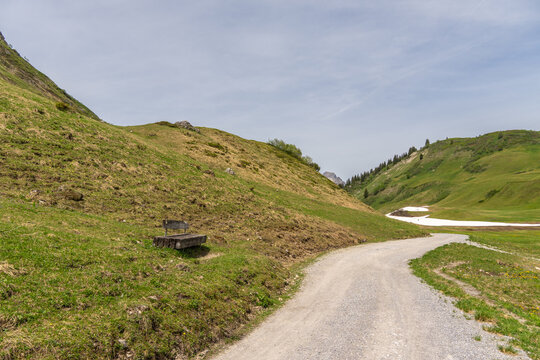 wooden park bench on slope near blue alpine lake in spring between forested mountains. hiking area in Bregenz forest, Vorarlberg, Austria. holiday destination for hike and skiing