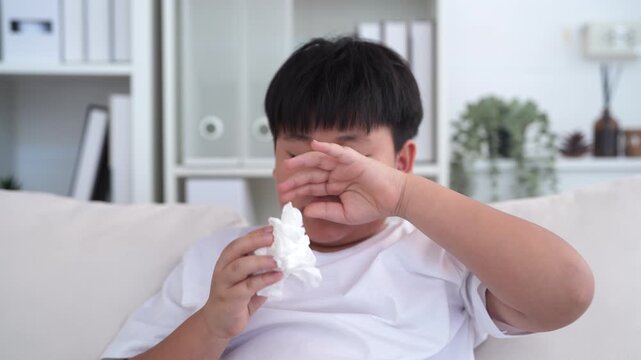 Young asian boy sneezing or blowing his nose and mouth with tissue, cold allergies or illness, health, virus and flu season, RSV, Influenza, childcare and hygiene practices, especially for children