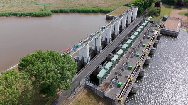 Close-up aerial view of a civil engineering tail sluice, flood defense barrier, and river water management system near King's Lynn, UK.