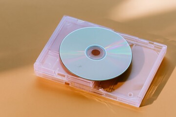 Fototapeta premium Iridescent blank CD disc on a pink plastic jewel case, glowing and luminous on a warm amber surface for media and music mockup concepts