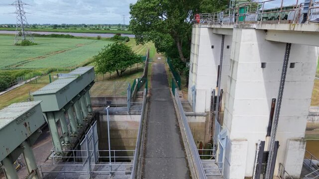 Close-up aerial view of a civil engineering tail sluice, flood defense barrier, and river water management system near King's Lynn, UK.