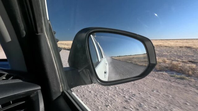 View in rear view mirror while driving through arid dry dusty road landscape in  Namibia