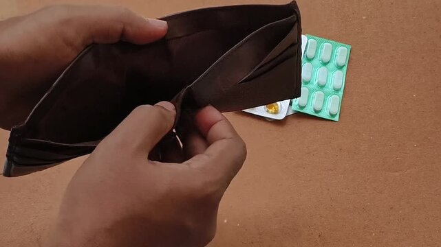 Poor broke person hands open empty wallet for money to buy medicine drug blisters. Health disparity, medical debt, expensive treatment cost, overpriced medications and unaffordable healthcare concept.